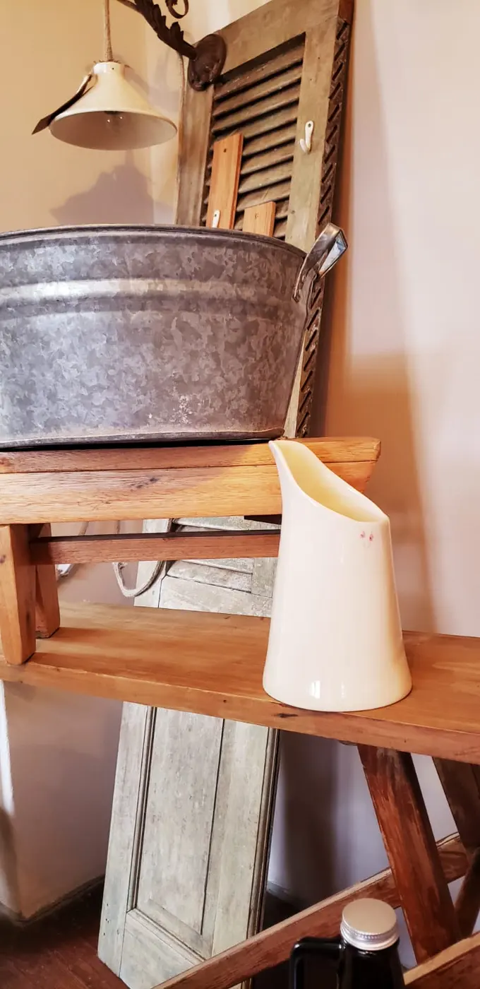 Jarra de cerámica color crema sobre un banco de madera, junto a un fuentón de chapa