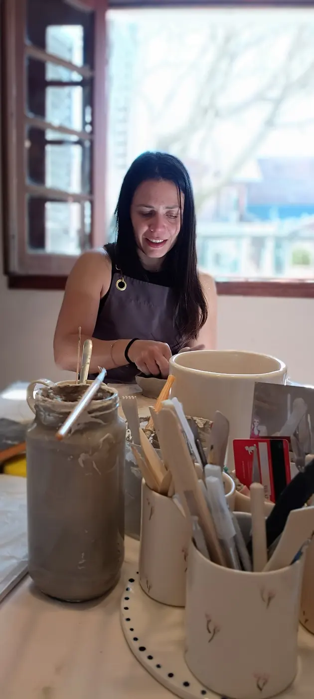 Una alumna sonriendo mientras trabaja el barro en la mesa del taller
