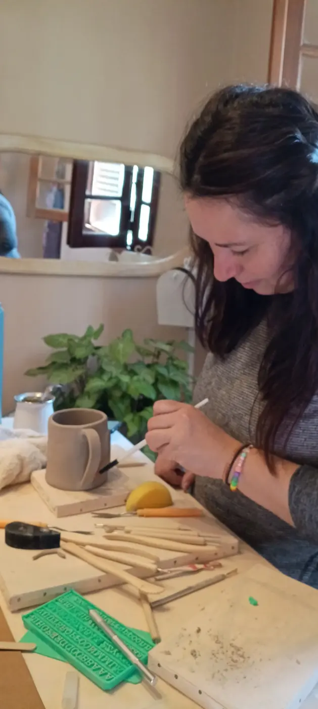 Una alumna modelando una taza de cerámica con herramientas finas